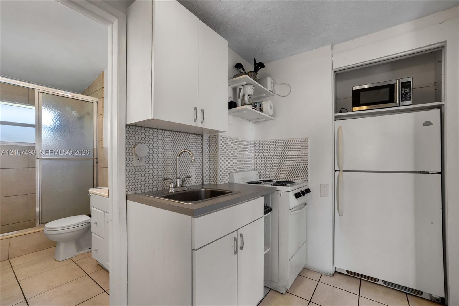 Compact kitchen featuring white cabinetry, hexagonal tile backsplash, stainless steel sink with arch faucet, and light-tone floor tiling