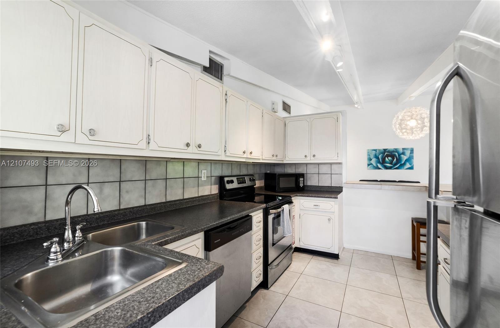 Kitchen featuring white cabinetry, dark stone-composite countertops, stainless steel appliances, a double-basin stainless steel sink, and ceramic tile flooring