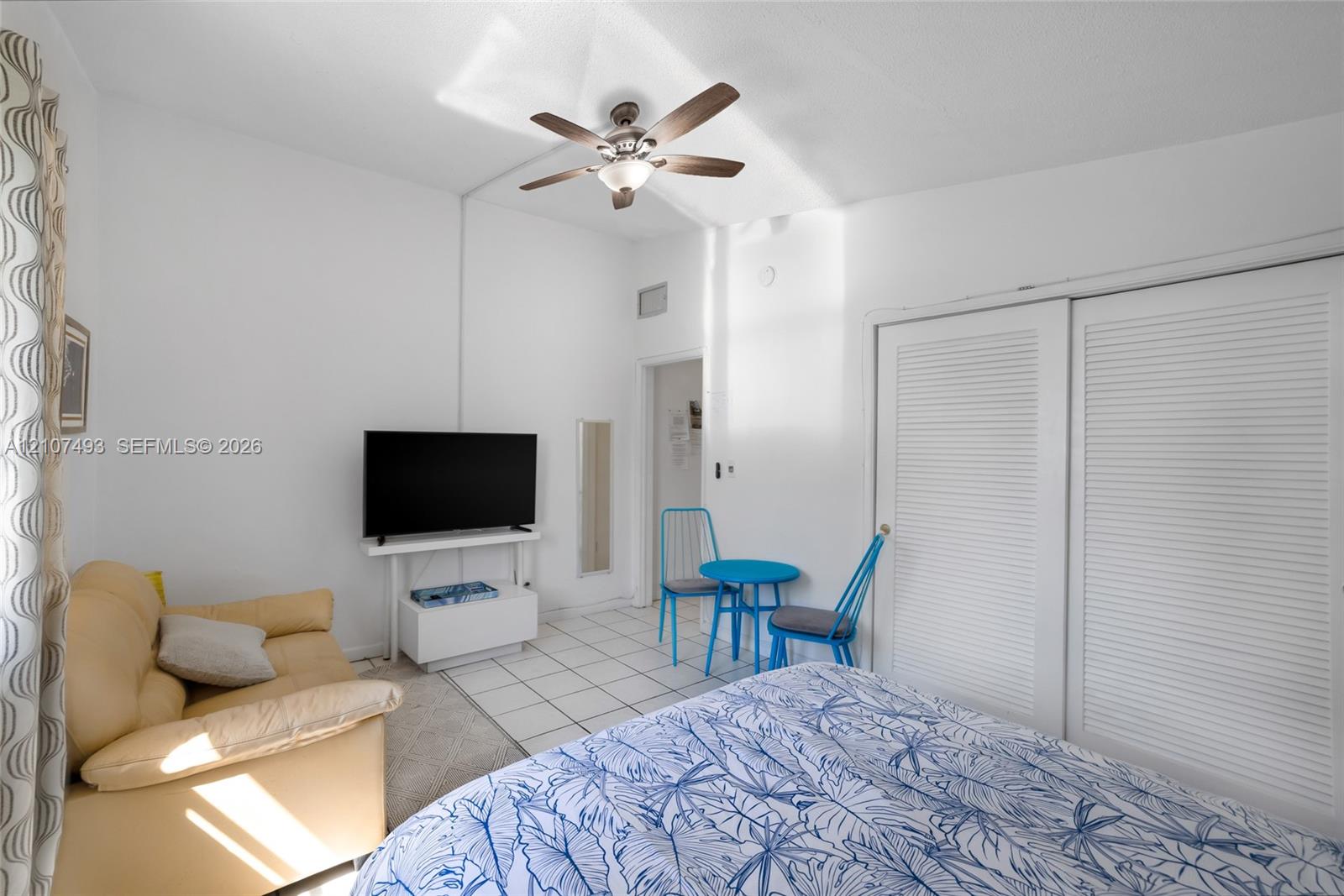High ceilings featuring a central ceiling fan with integrated light fixture, ceramic tile flooring, and dual white louvered closet doors