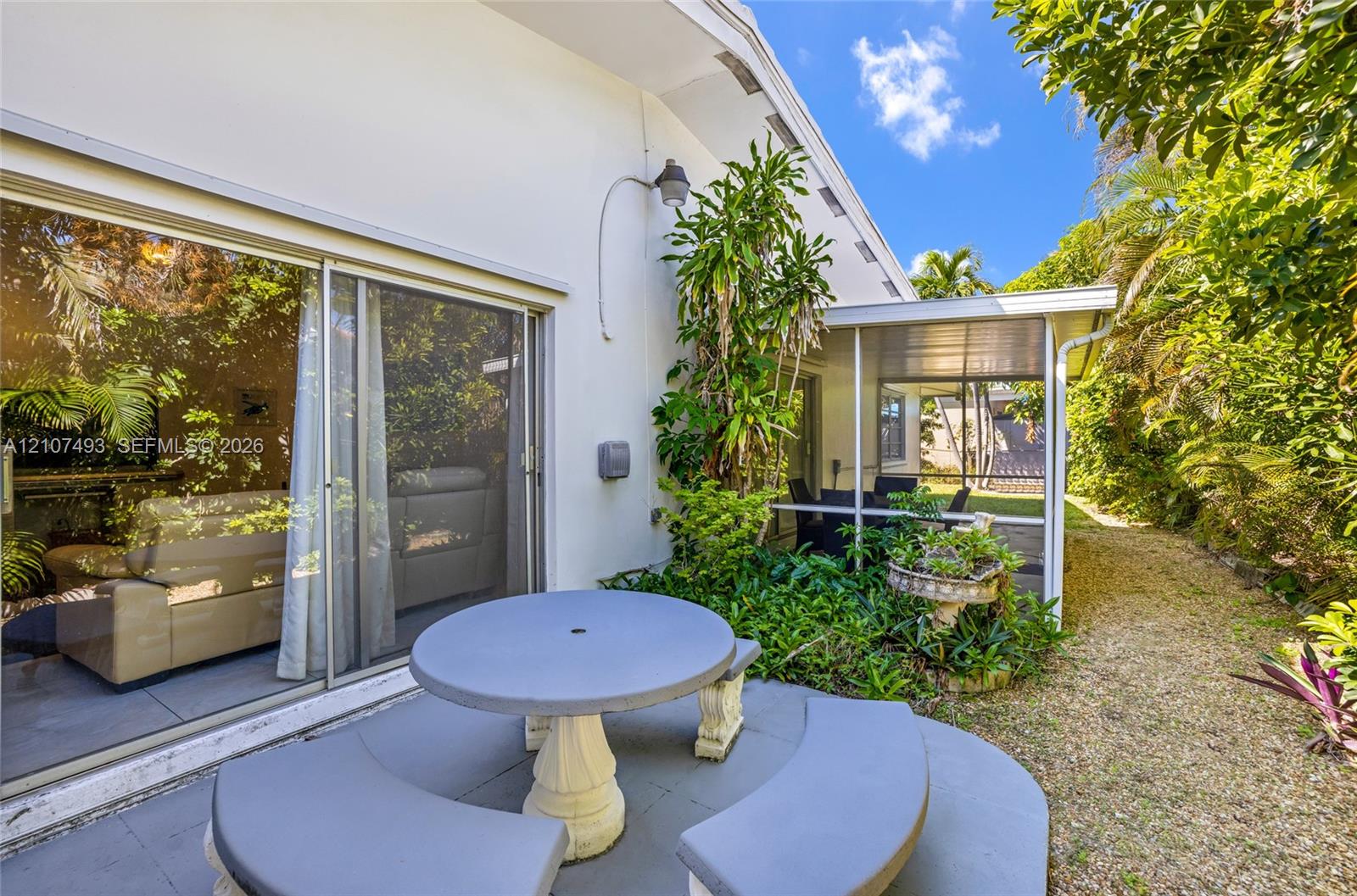 Exterior patio featuring a concrete dining table with curved benches, sliding glass doors, and a screened-in lanai