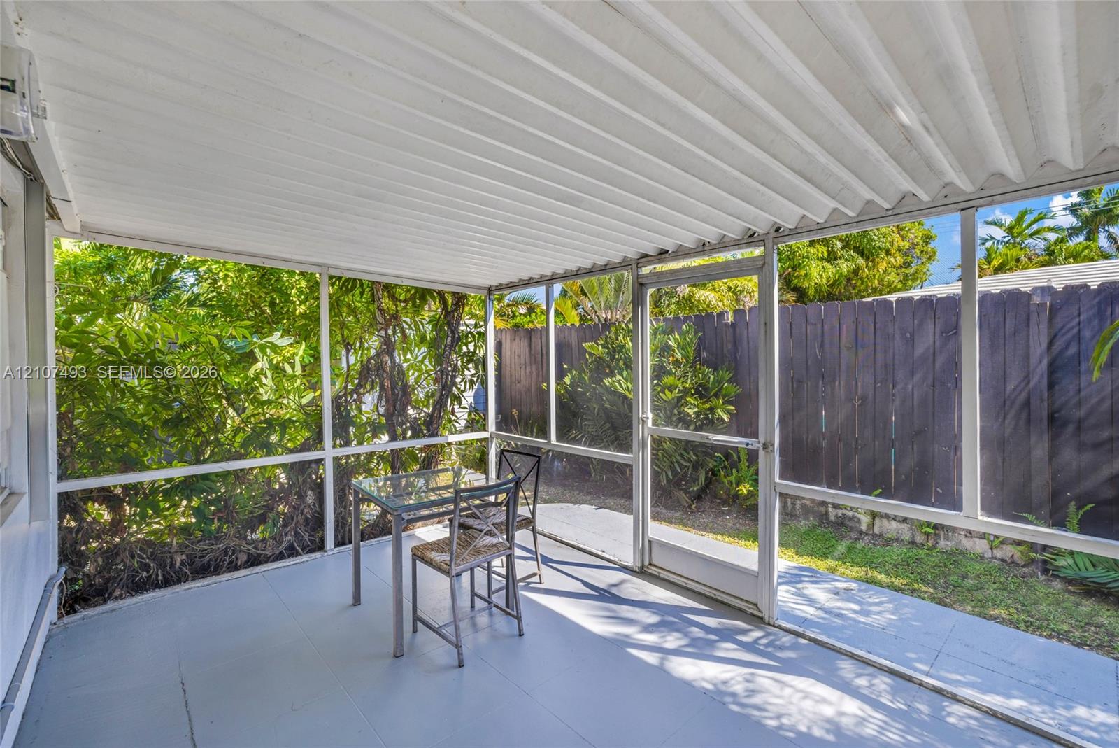 Screened-in porch featuring a corrugated metal roof, aluminum framing, solid flooring, and a private wooden fence perimeter