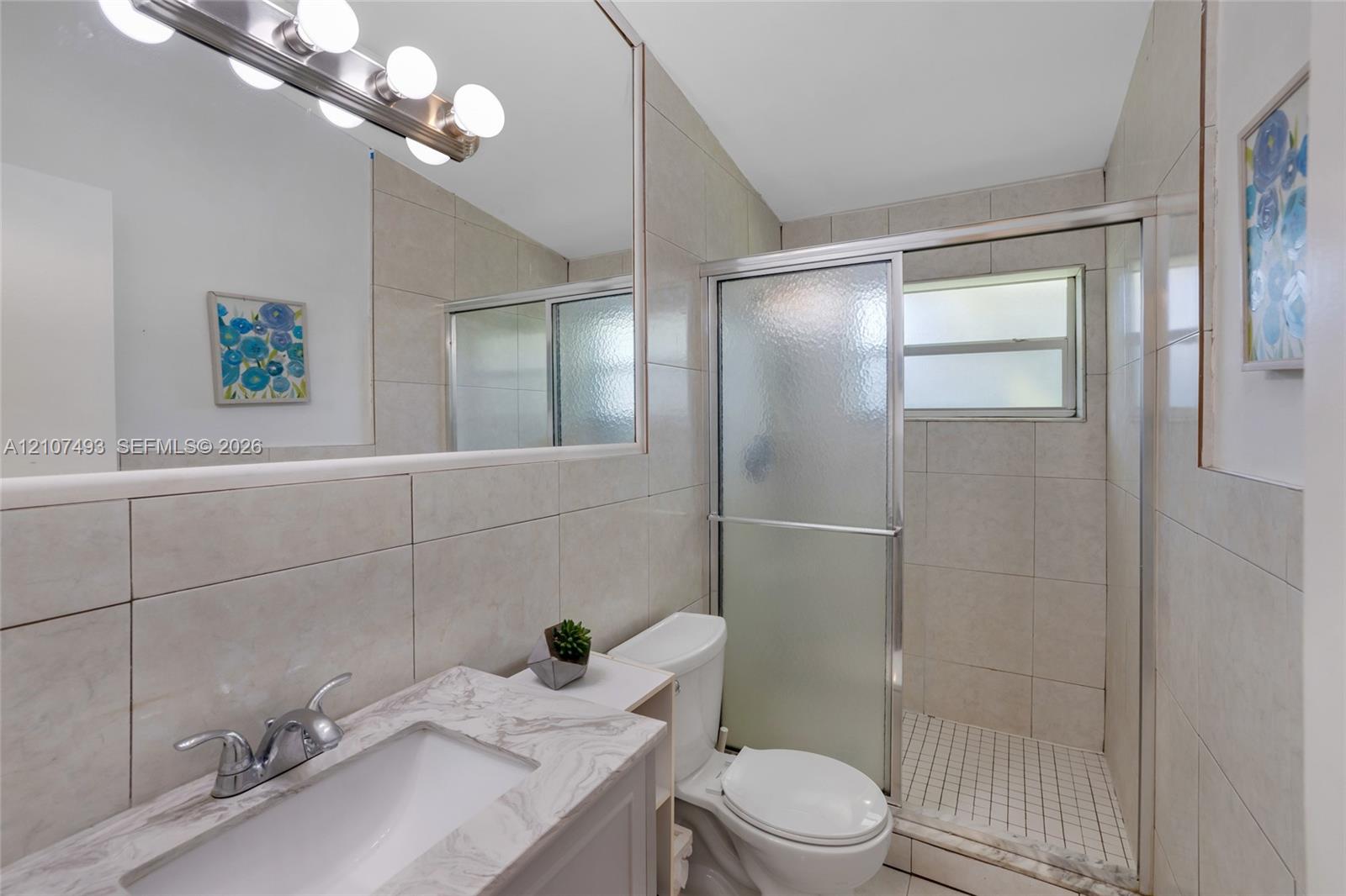 Bathroom featuring a stone-finish countertop, undermount sink, full-width vanity mirror, six-light fixture, and a tiled shower enclosure with sliding glass doors