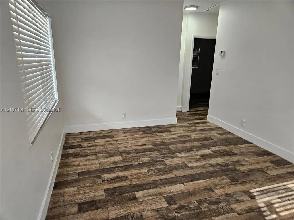 Interior space featuring wood-finish flooring, white walls, and a window equipped with horizontal blinds Interior space featuring wood-finish flooring, white walls, and a window equipped with horizontal blinds