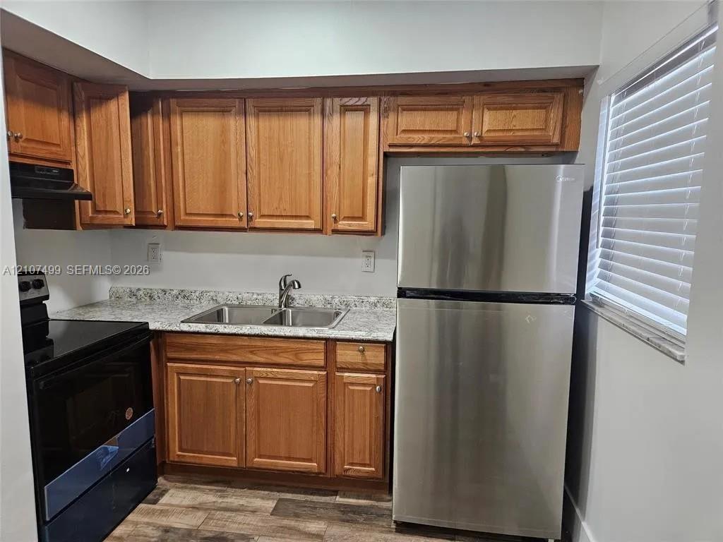 Kitchen featuring wood cabinetry, stone-finish countertops, stainless steel refrigerator, dual-basin sink, and wood-finish flooring Kitchen featuring wood cabinetry, stone-finish countertops, stainless steel refrigerator, dual-basin sink, and wood-finish flooring