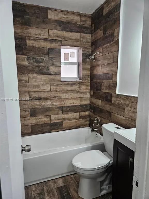 Bathroom featuring wood-finish wall tiling, white porcelain bathtub, wall-mounted showerhead, and dark cabinetry with an integrated basin Bathroom featuring wood-finish wall tiling, white porcelain bathtub, wall-mounted showerhead, and dark cabinetry with an integrated basin