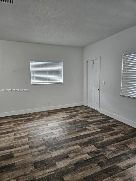 Interior room featuring wood-finish flooring, white walls, and two windows equipped with horizontal blinds Interior room featuring wood-finish flooring, white walls, and two windows equipped with horizontal blinds