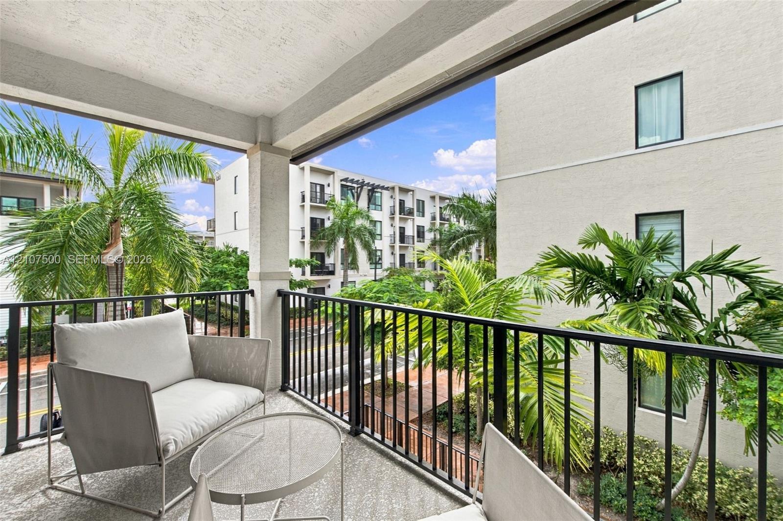Covered balcony featuring concrete flooring, black metal railing, and a textured stucco ceiling