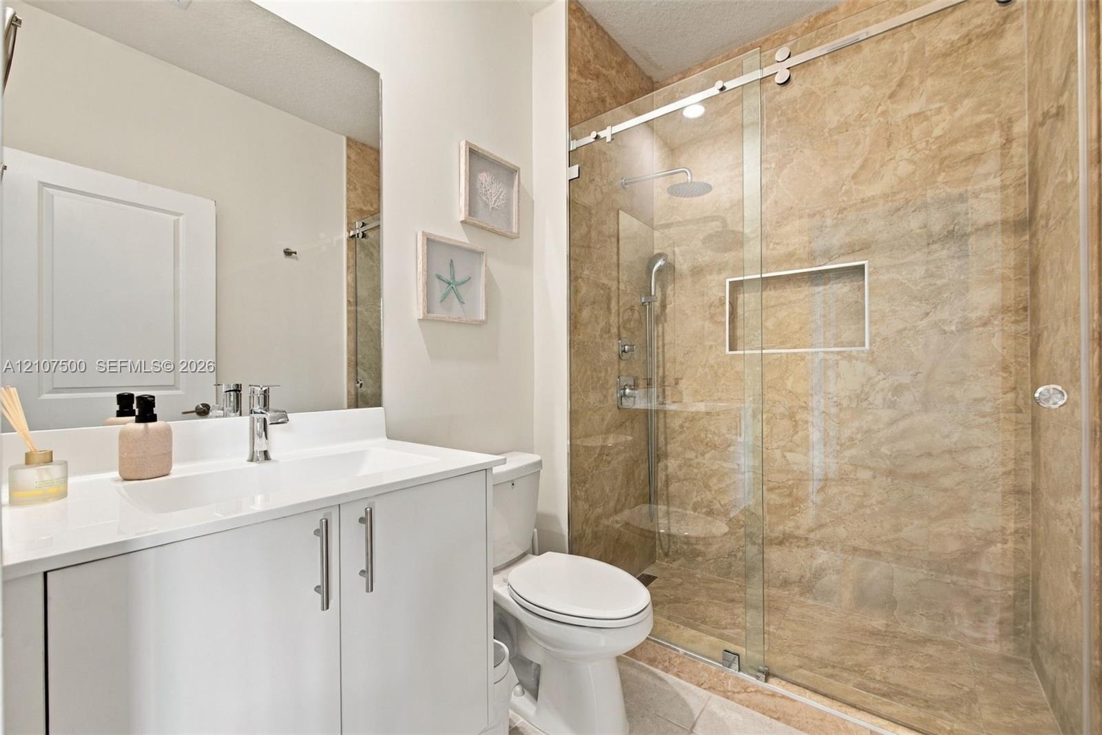 Bathroom featuring a white vanity with a rectangular sink, a frameless glass shower enclosure with sliding hardware, stone-finish wall tile, and a recessed shower niche
