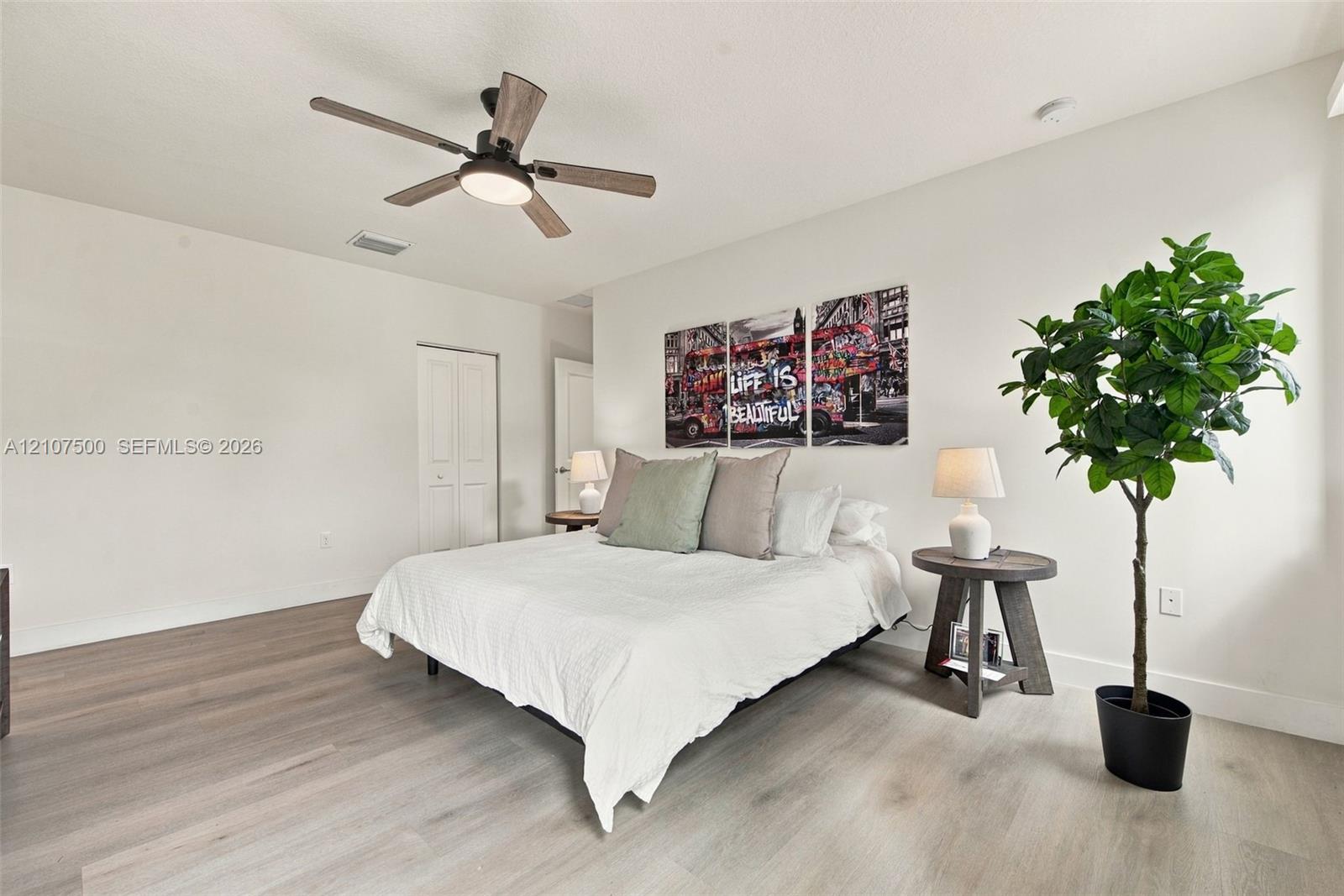 Neutral-toned room featuring wood-finish flooring, a multi-blade ceiling fan with integrated lighting, and white six-panel closet doors
