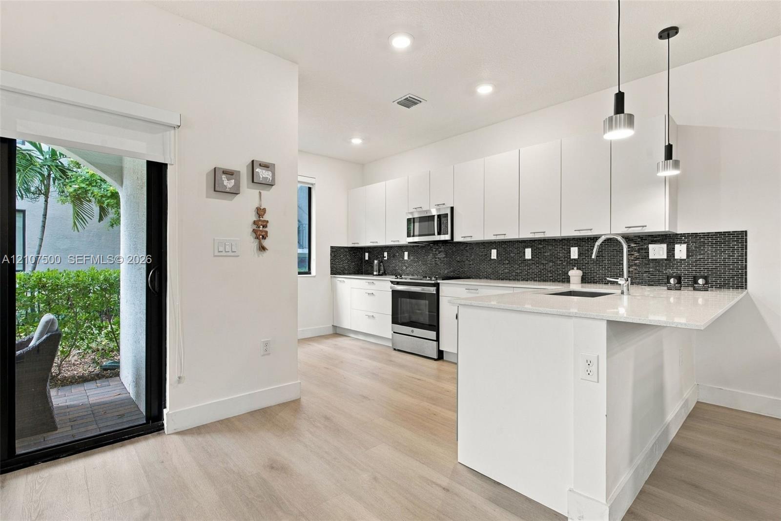 Kitchen featuring flat-panel white cabinetry, stone-finish countertops, stainless steel appliances, a dark mosaic tile backsplash, and wood-finish flooring