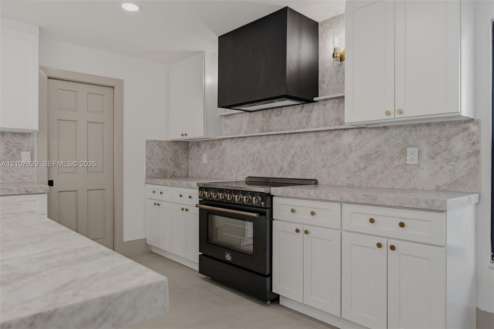 Kitchen featuring white shaker-style cabinetry, a large island with integrated microwave, stone-finish countertops and backsplash, black matte range with matching hood, and a multi-globe light fixture