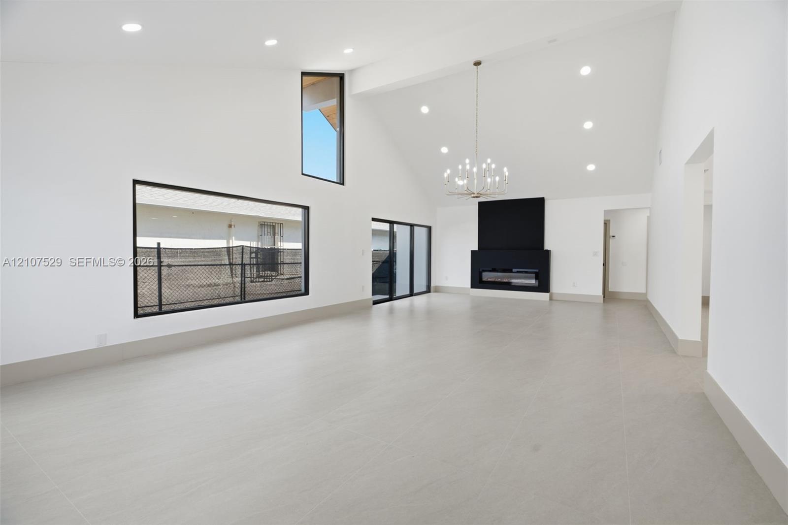 Vaulted ceilings featuring recessed lighting and a multi-tiered gold-tone chandelier, complemented by large-format neutral tile flooring and geometric paneled double entry doors