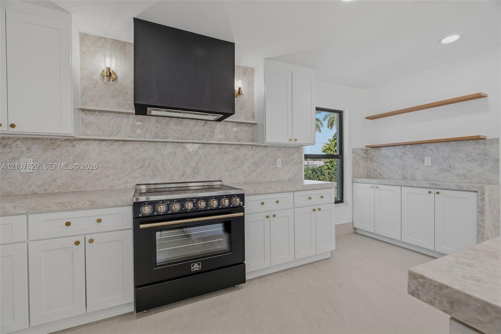 Kitchen featuring white shaker-style cabinetry, a contrasting matte black range hood, a dark finish freestanding range, and stone-surface countertops with matching full-height backsplash