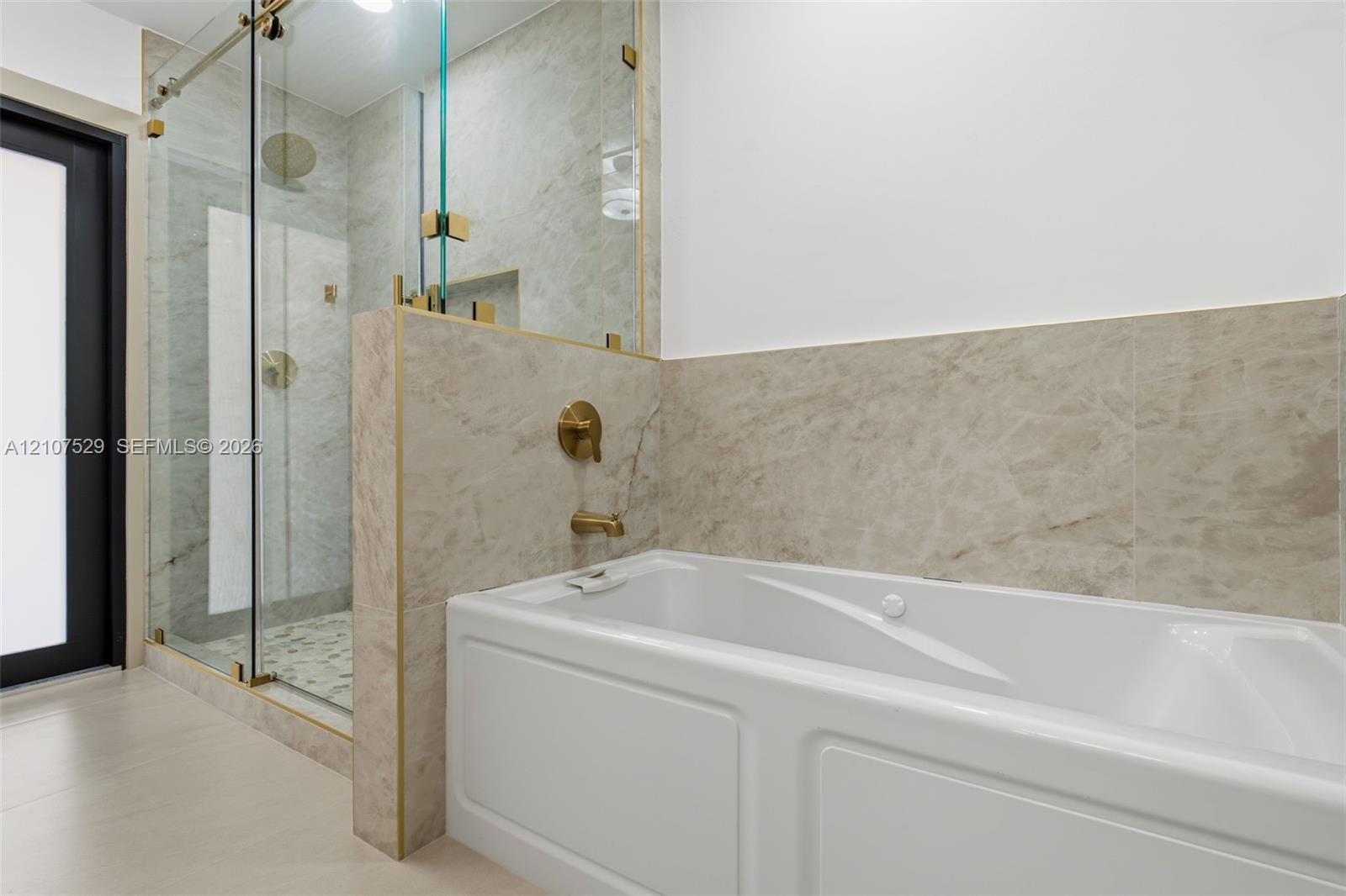 Walk-in shower featuring a glass enclosure, brass sliding hardware, a built-in recessed niche, and stone-finish tile surrounds with a river-stone shower floor, accompanied by a built-in soaking tub with brass fixtures