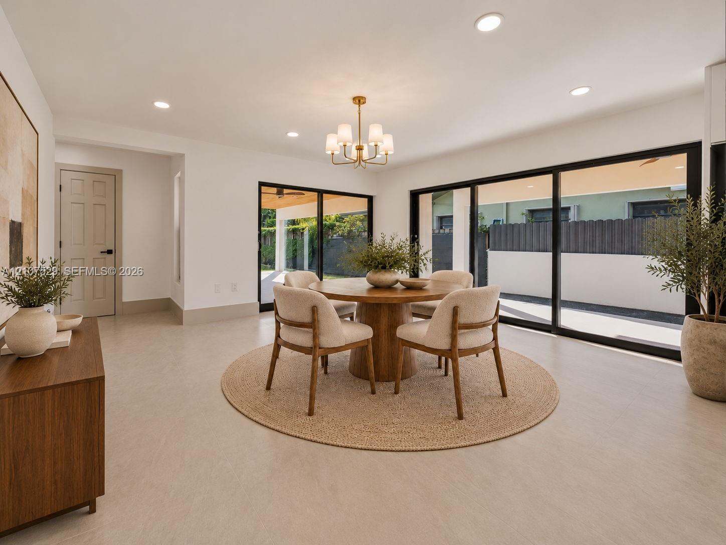 Neutral-toned interior featuring large-format flooring, recessed lighting, a multi-arm chandelier, and expansive sliding glass doors