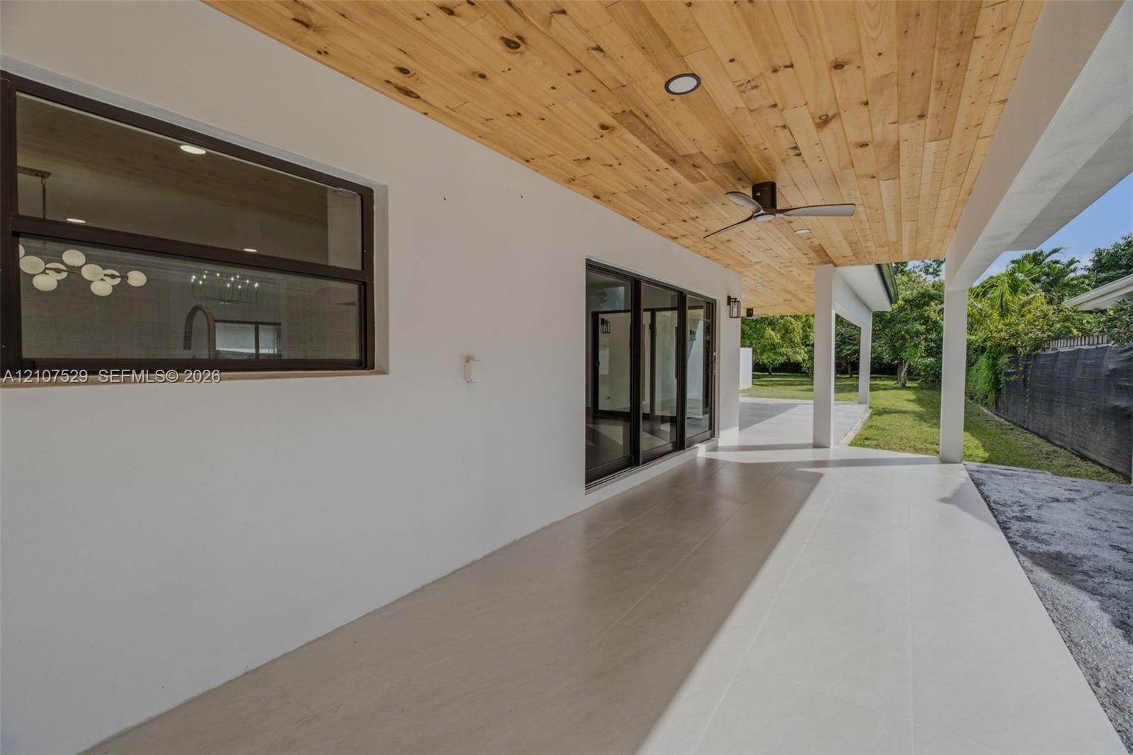 Covered patio featuring a wood-plank ceiling, ceiling fan, large sliding glass doors, and light-toned tile flooring