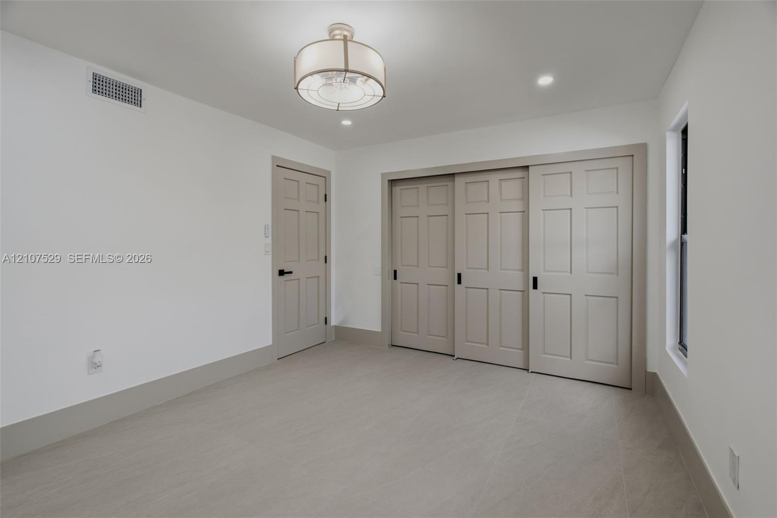 Neutral interior featuring large-format tile flooring, drum-style ceiling light fixture, recessed lighting, and windows with black frames