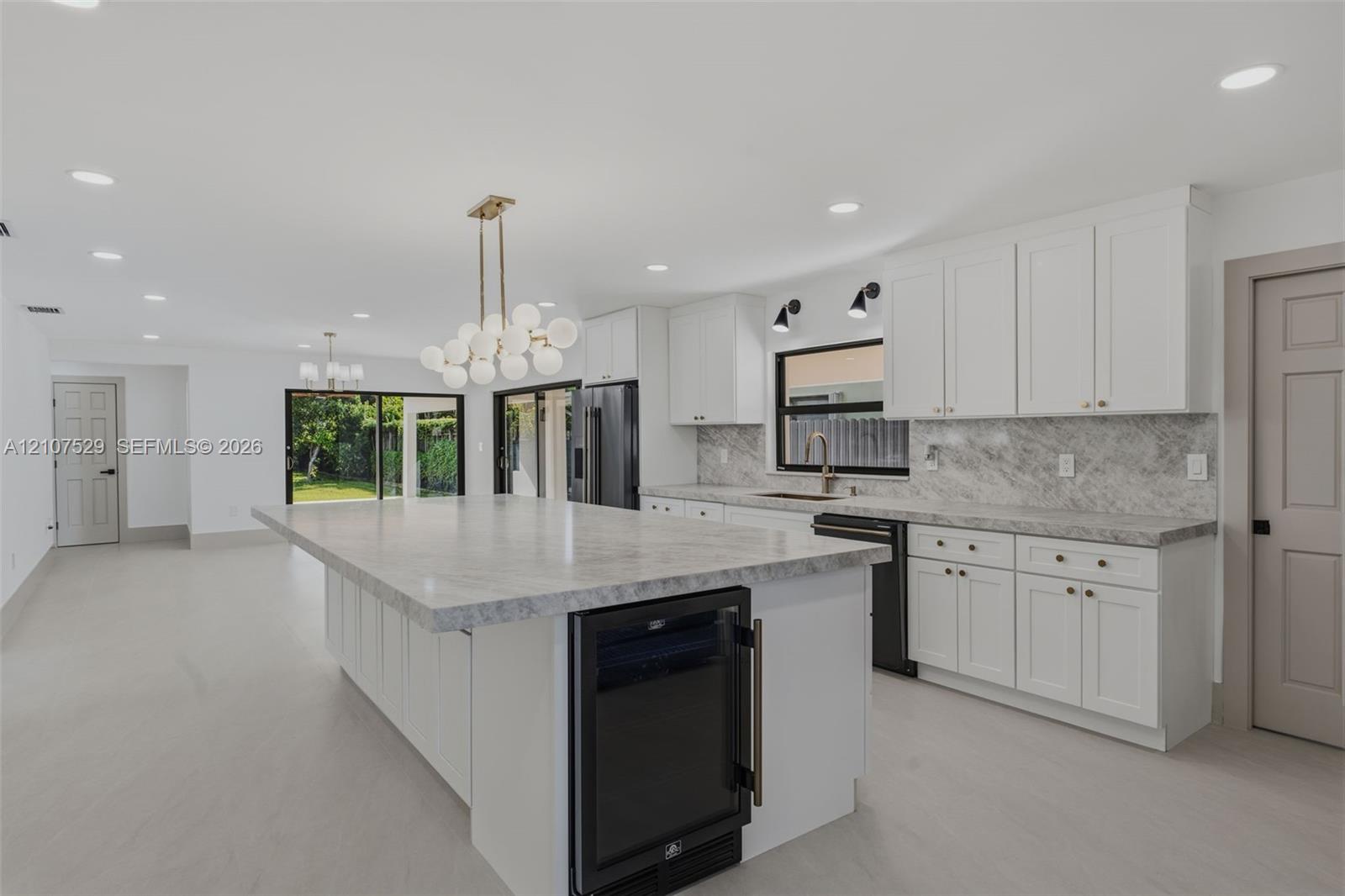 Large kitchen island with a stone-surface countertop, white Shaker-style cabinetry, matte gold-finish hardware, built-in microwave oven, and a contemporary multi-globe linear chandelier