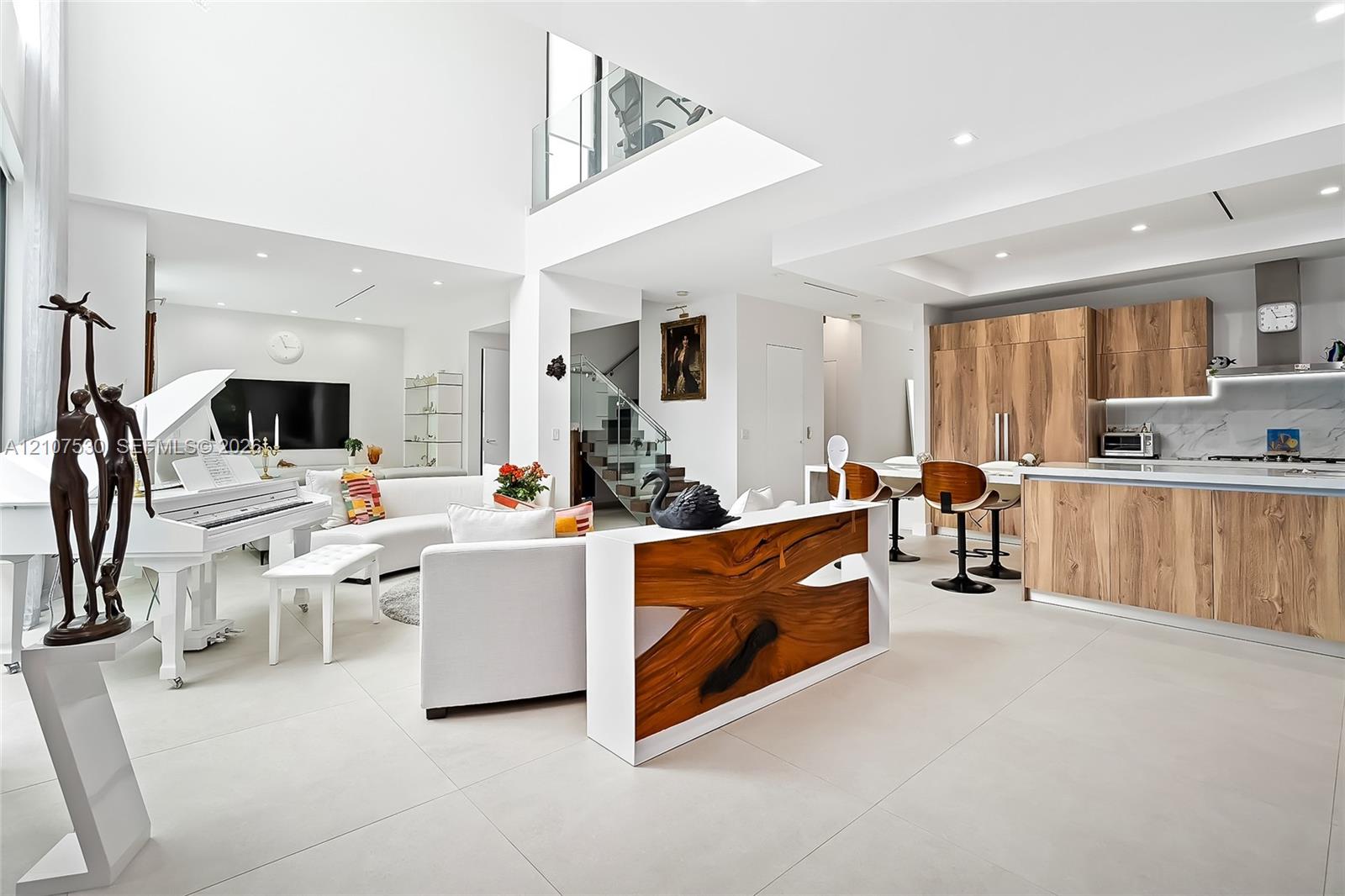 Double-height ceiling, large-format tile flooring, recessed lighting, and kitchen cabinetry featuring a wood finish with a stone-style backsplash
