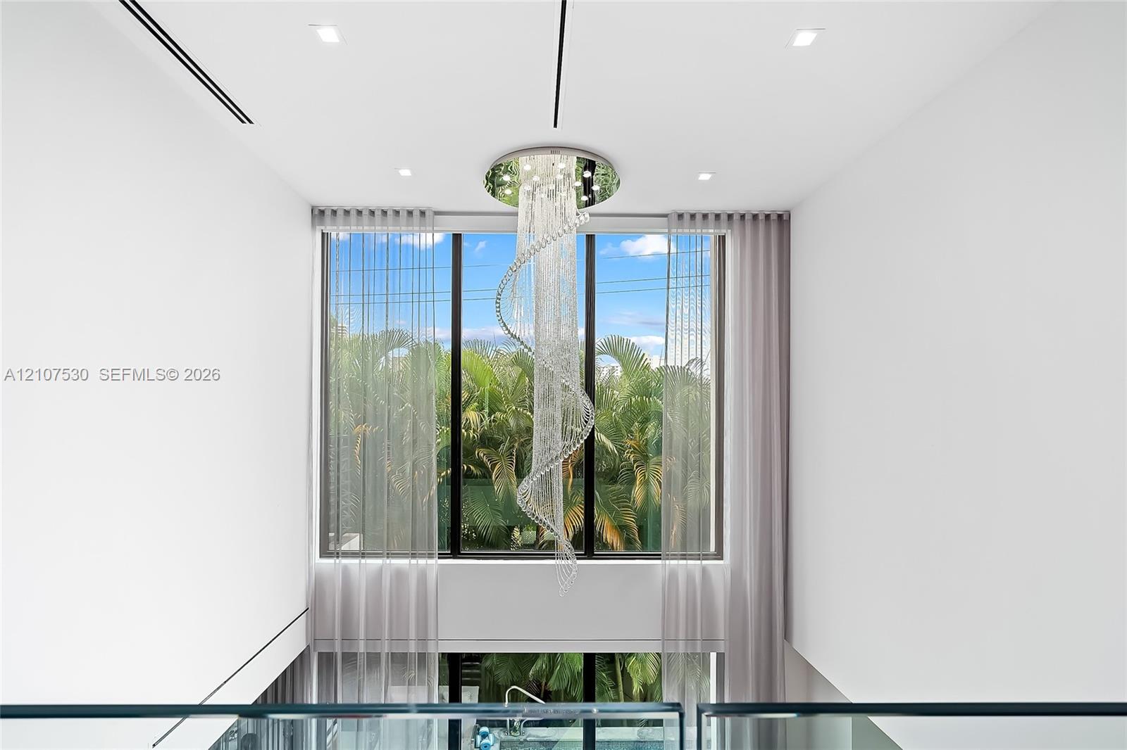 Floor-to-ceiling windows featuring a spiral crystal chandelier, recessed ceiling lighting, and a glass panel railing