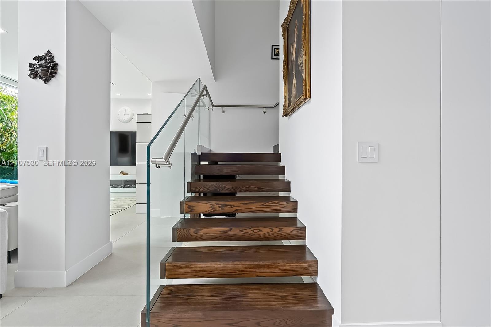 Floating staircase featuring rich wood treads, glass panel railings, and a stainless steel handrail