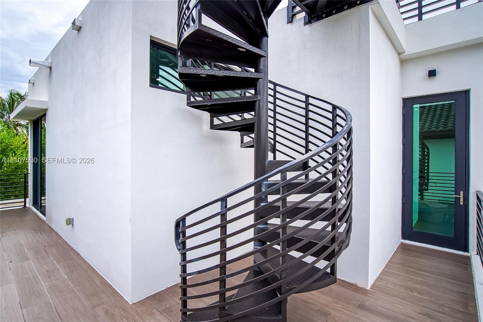 Black metal spiral staircase featuring open-riser treads, wood-finish flooring, and a glass-paneled entry door