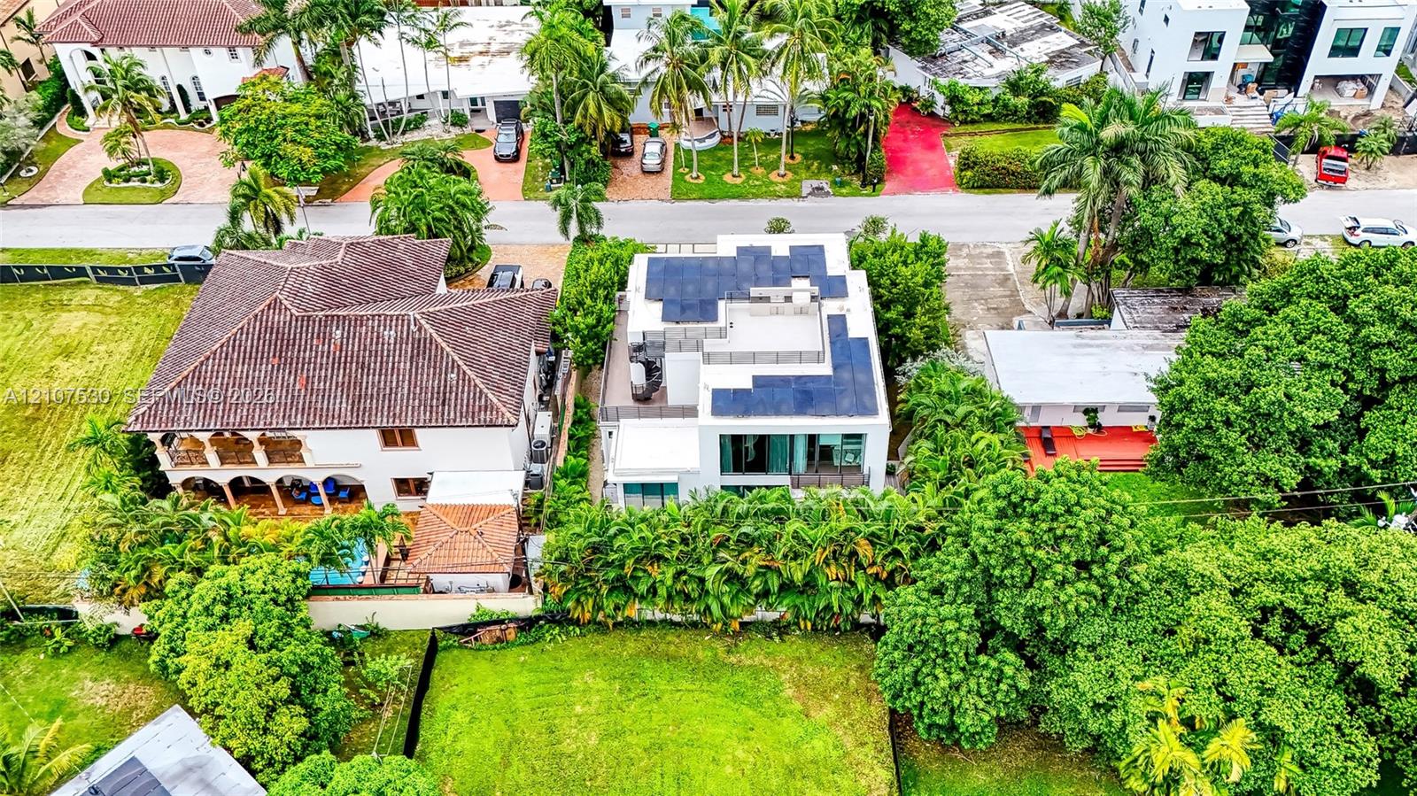 Aerial perspective of a multi-level contemporary residence featuring integrated solar panel arrays, a flat roofline, floor-to-ceiling glass paneling, and dense perimeter landscaping
