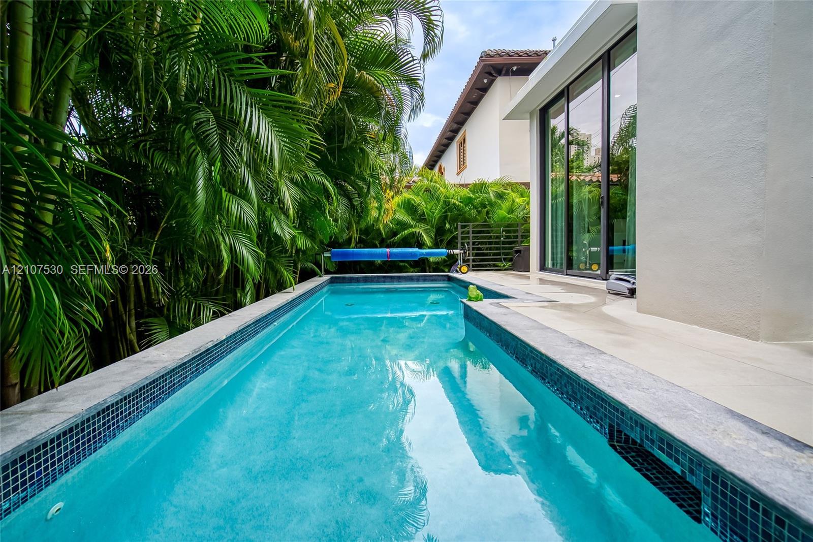 Rectangular lap pool featuring dark mosaic tile trim, concrete decking, and floor-to-ceiling sliding glass doors