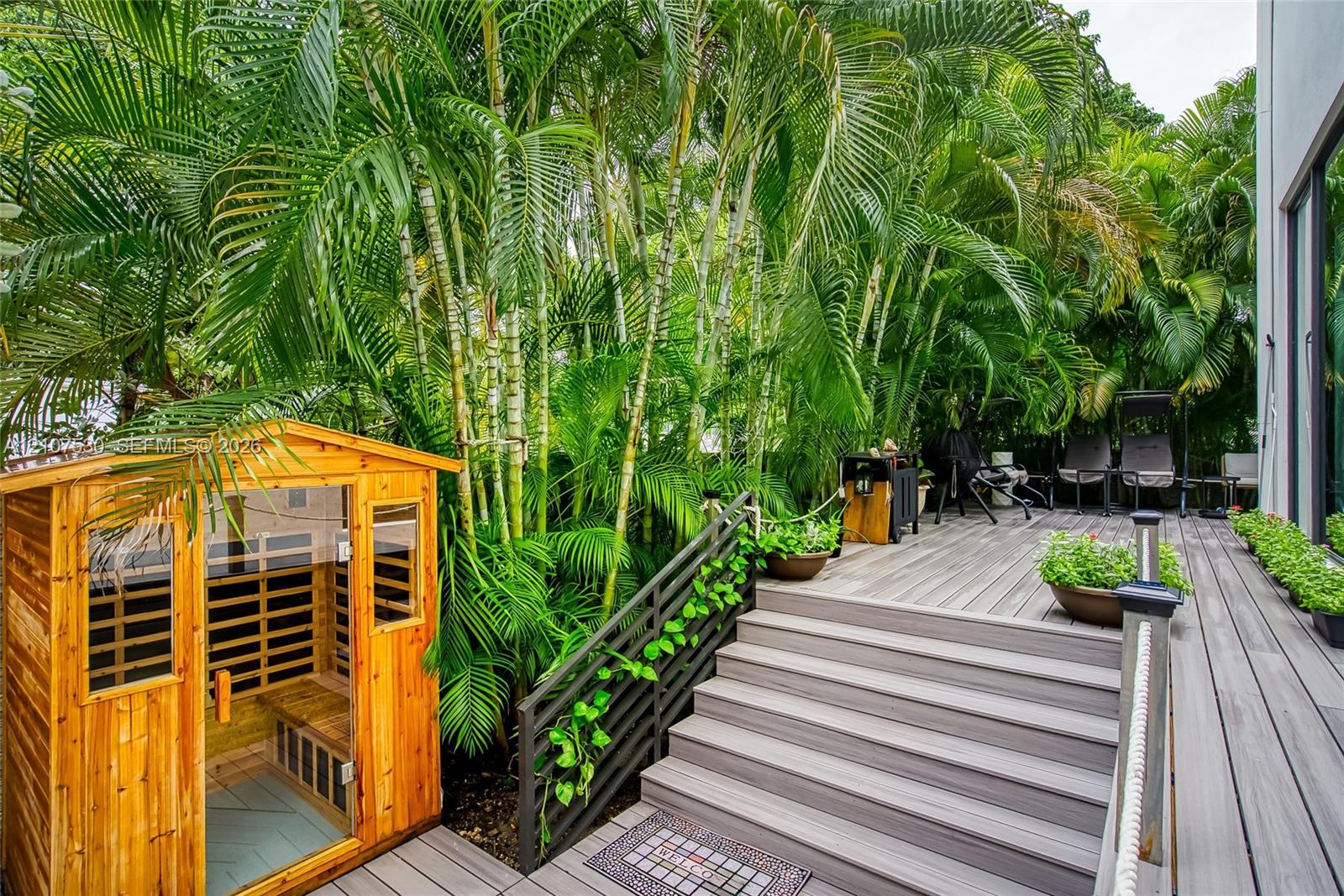 Multi-level composite decking, built-in wooden sauna, black metal railings, and dense mature palm landscaping