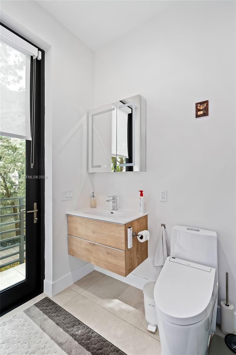 Wall-mounted vanity featuring wood-finish cabinetry and a white countertop, mirrored medicine cabinet, integrated sink faucet, and tile flooring