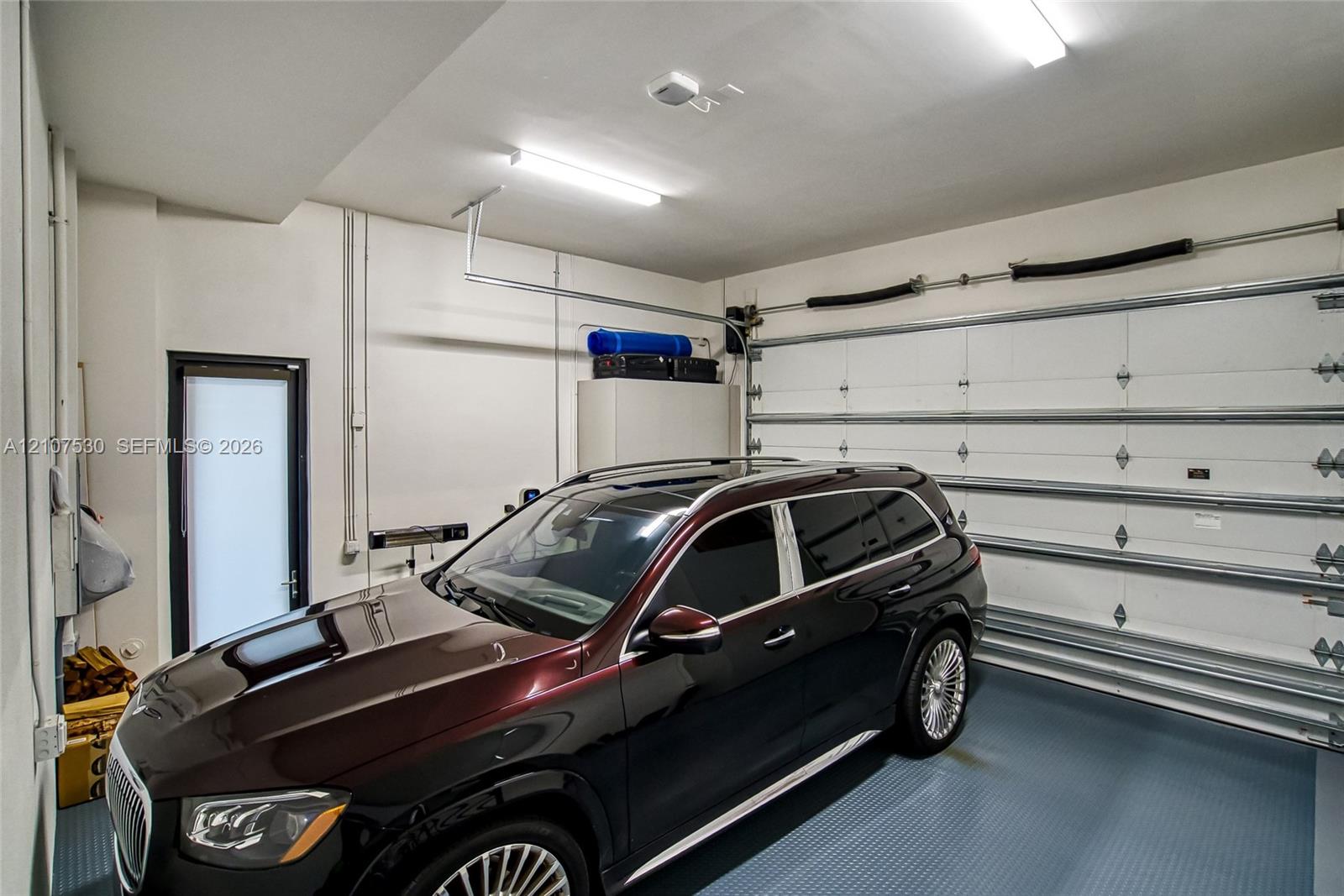 Enclosed garage featuring a metal sectional door, textured epoxy flooring, fluorescent lighting, and a pedestrian door
