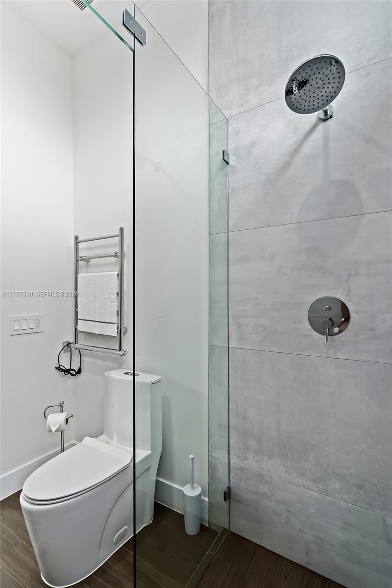 Walk-in glass shower enclosure featuring large-format tile surround, rainfall showerhead, wall-mounted towel warmer, and wood-finish flooring