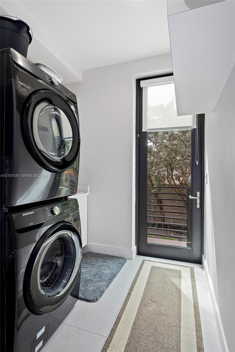 Laundry area featuring stacked appliances, a solid-surface countertop, cabinetry, and a full-height glass-panel door