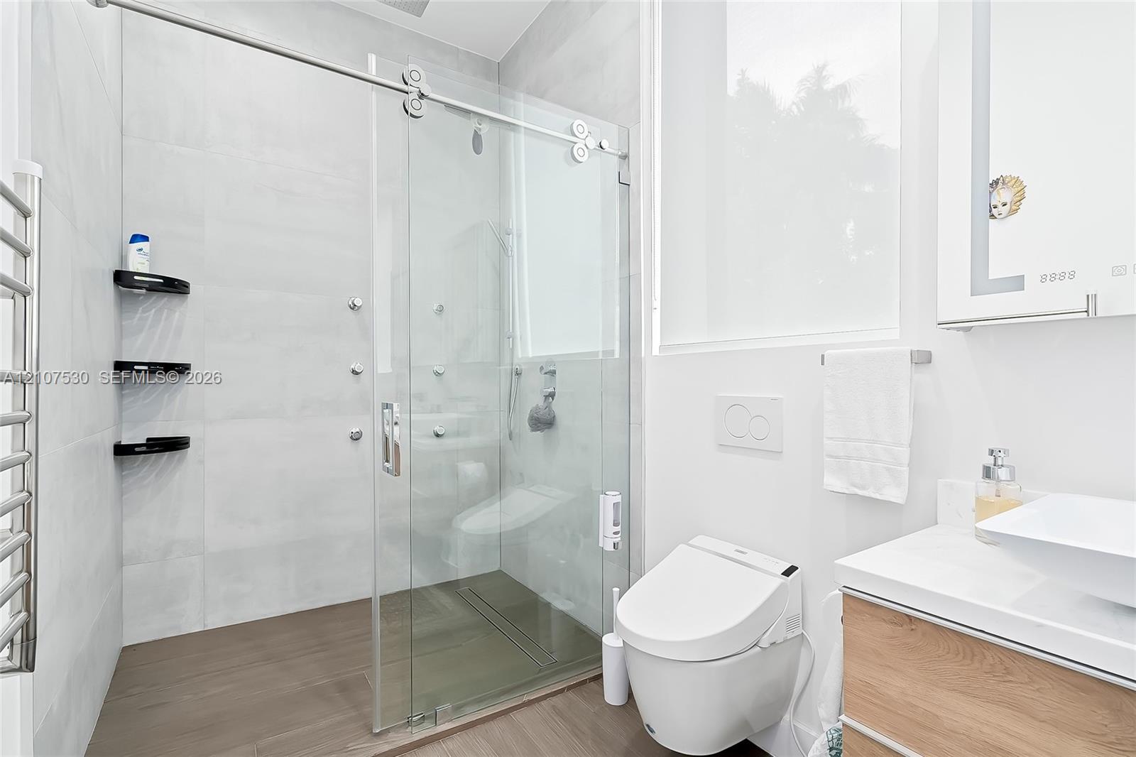 Walk-in shower featuring a sliding glass door, multi-head shower system, built-in shelving, and wood-finish flooring
