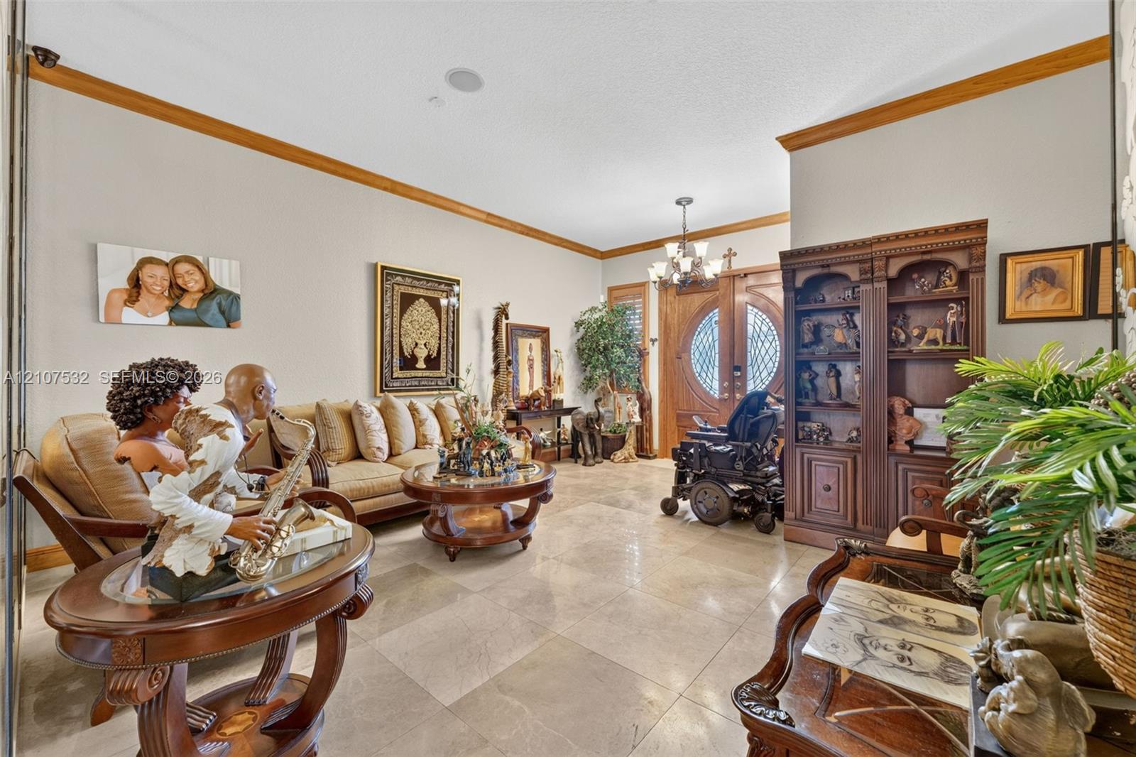 Large-format tile flooring, crown molding, built-in wooden cabinetry, multi-light chandelier, and double-entry doors with decorative glass inserts