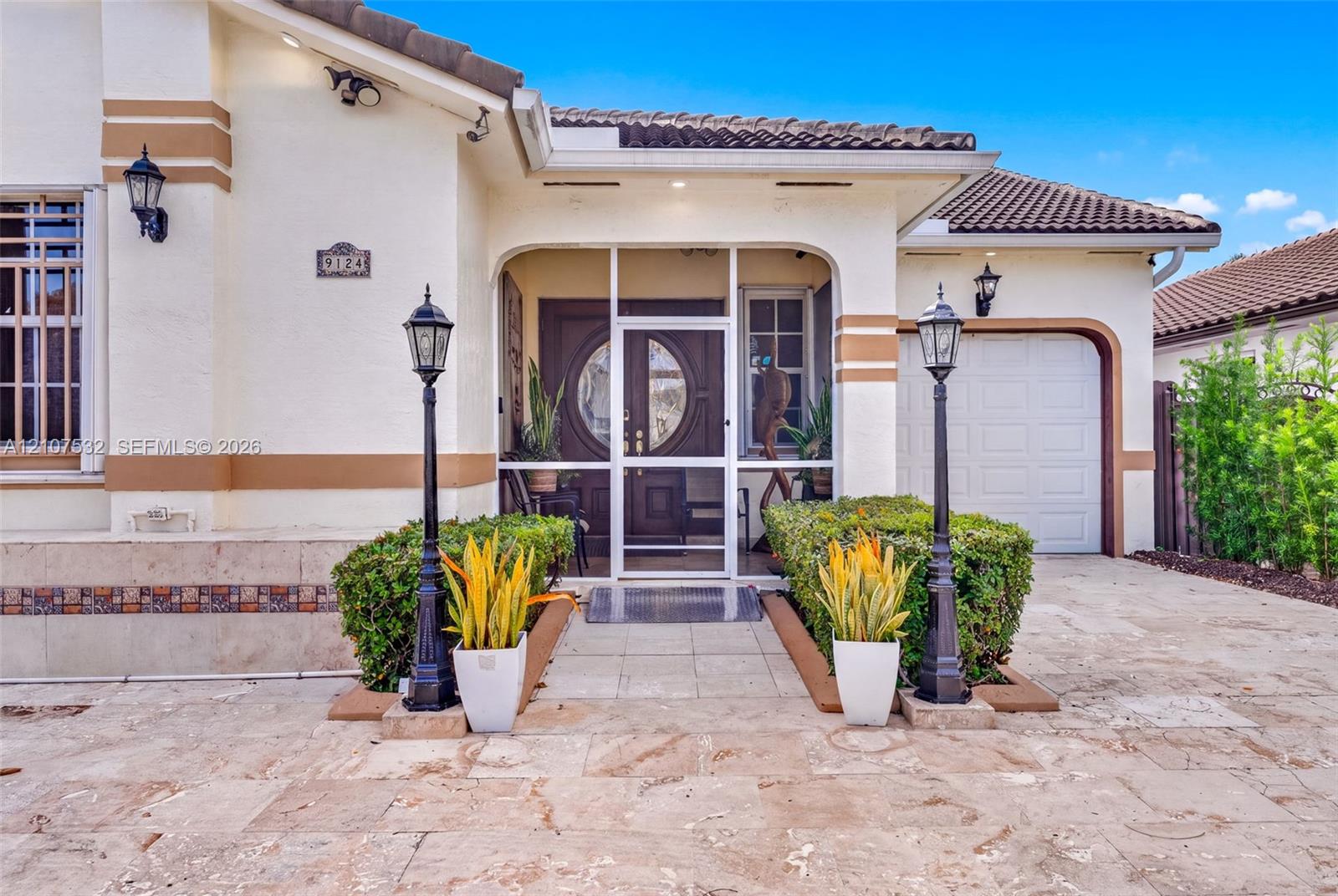 Stucco exterior featuring a tiled roof, arched entryway with a screened enclosure, ornamental iron lamp posts, and stone-finish paved driveway Stucco exterior featuring a tiled roof, arched entryway with a screened enclosure, ornamental iron lamp posts, and stone-finish paved driveway