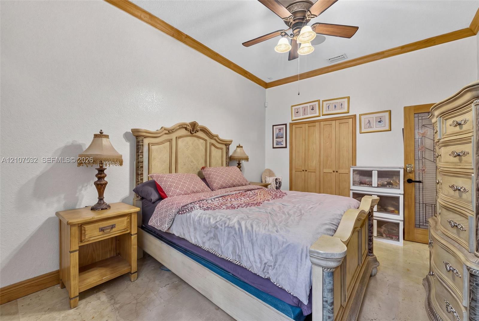 Vaulted ceiling featuring crown molding, neutral stone-finish flooring, ceiling fan with integrated light fixture, built-in wooden closet doors, and a door with decorative glass paneling Vaulted ceiling featuring crown molding, neutral stone-finish flooring, ceiling fan with integrated light fixture, built-in wooden closet doors, and a door with decorative glass paneling
