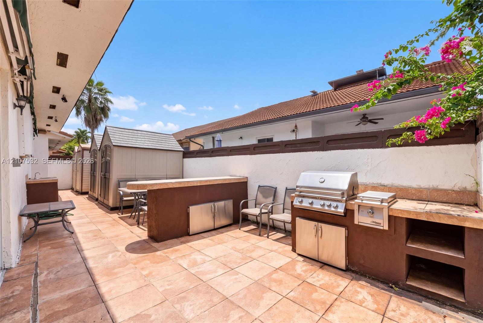 Outdoor kitchen featuring a built-in stainless steel grill, stone-finish countertops, tiled patio flooring, and stucco wall enclosure