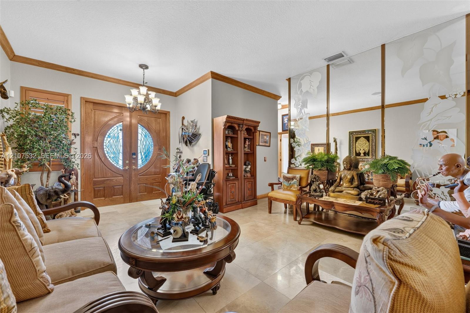 Entryway featuring double wood doors with circular glass inserts, tile flooring, crown molding, a decorative multi-arm chandelier, and full-wall mirrored paneling