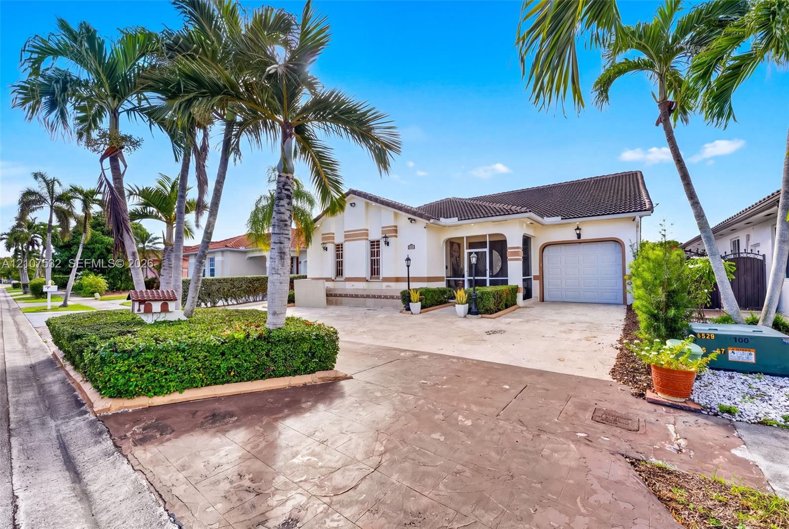 Single-story exterior featuring a light-toned stucco faade, a tiled roof, an attached garage, and mature palm trees Single-story exterior featuring a light-toned stucco faade, a tiled roof, an attached garage, and mature palm trees