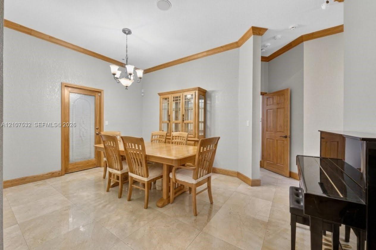 Stone tile flooring, crown molding, a decorative glass-panel door, and a multi-arm chandelier