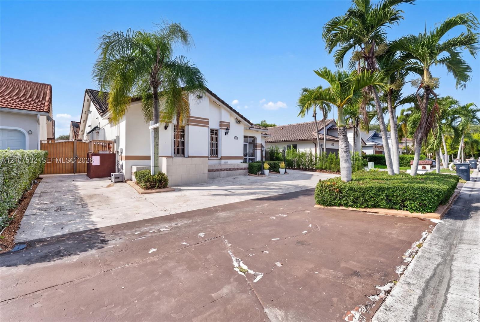 Stucco exterior with horizontal detailing, concrete paved driveway, wood-finish privacy gate, and manicured palm tree landscaping Stucco exterior with horizontal detailing, concrete paved driveway, wood-finish privacy gate, and manicured palm tree landscaping