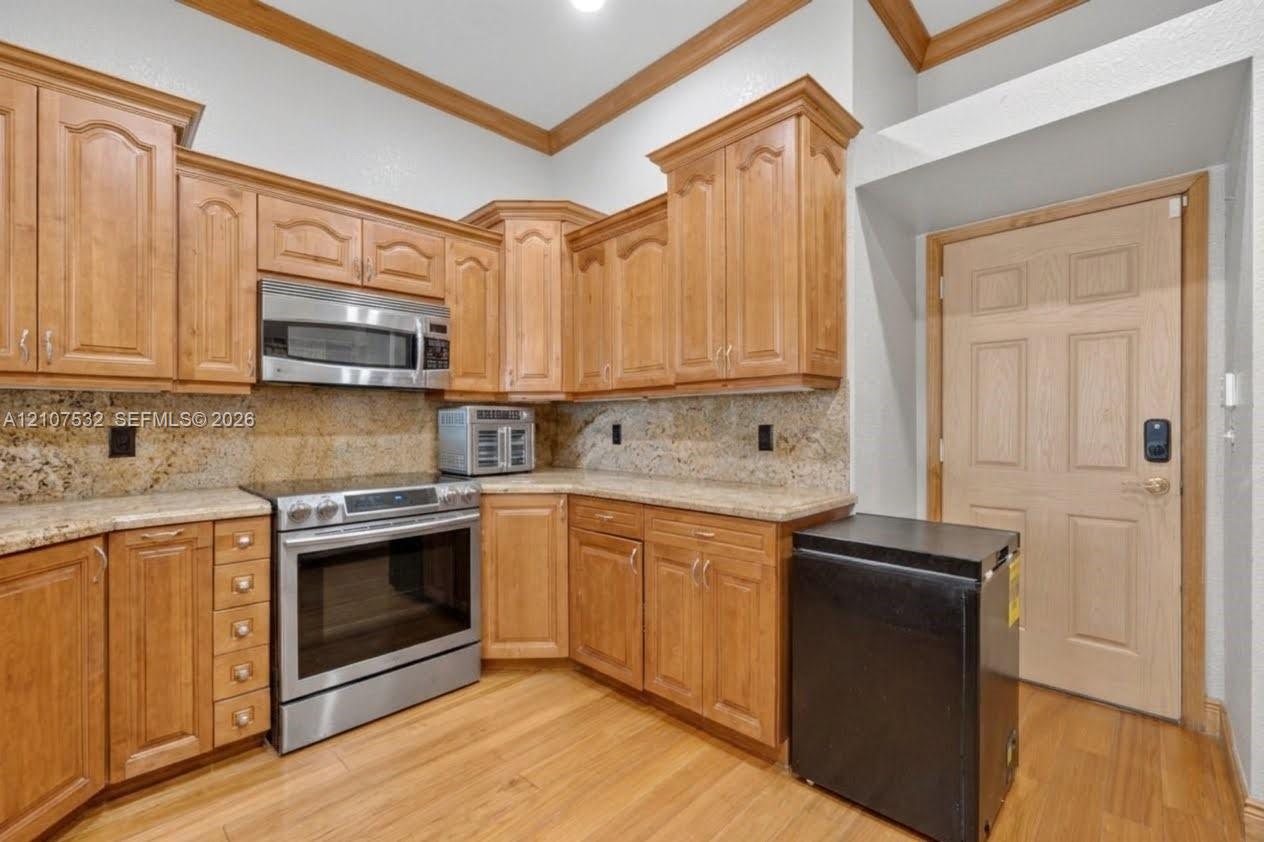 Kitchen featuring natural finish wood cabinetry, stone countertops, stainless steel appliances, crown molding, and wood-finish flooring
