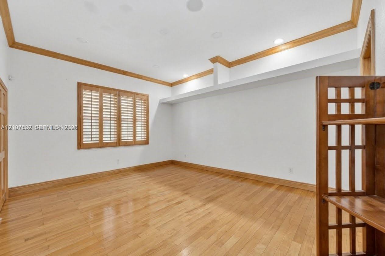 Interior space featuring wood-finish flooring, ceiling crown molding, wood-framed window shutters, recessed lighting, and a built-in recessed shelf