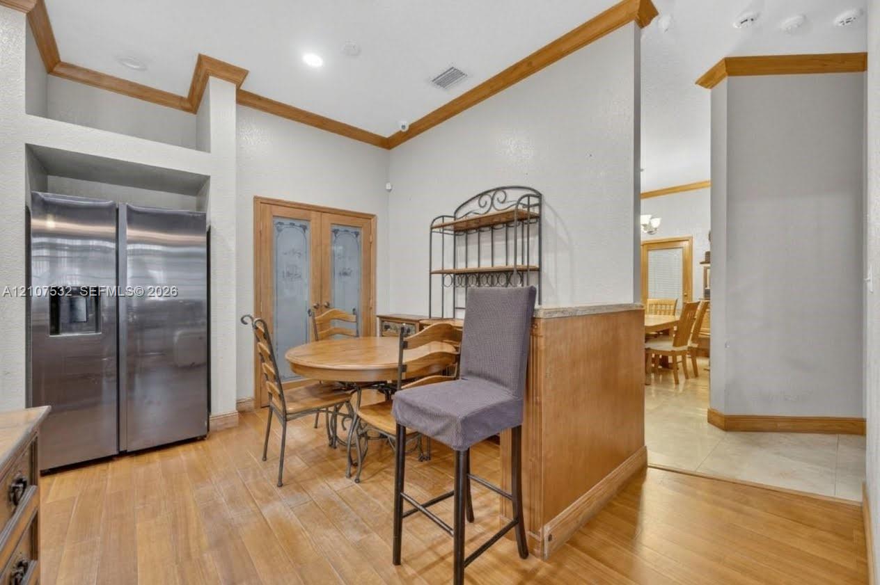 Stainless steel side-by-side refrigerator, wood-finish flooring, recessed lighting, crown molding, and glass-paneled double doors
