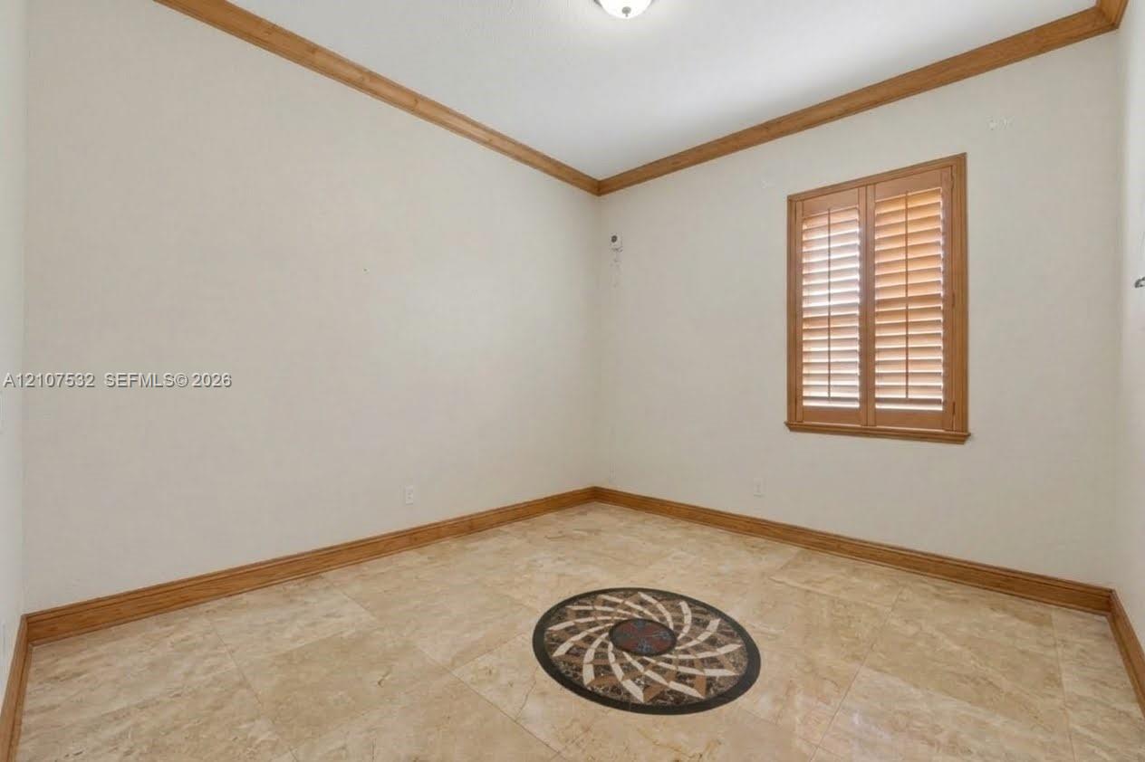 Interior room featuring stone flooring with a circular medallion inlay, crown molding, and plantation shutters