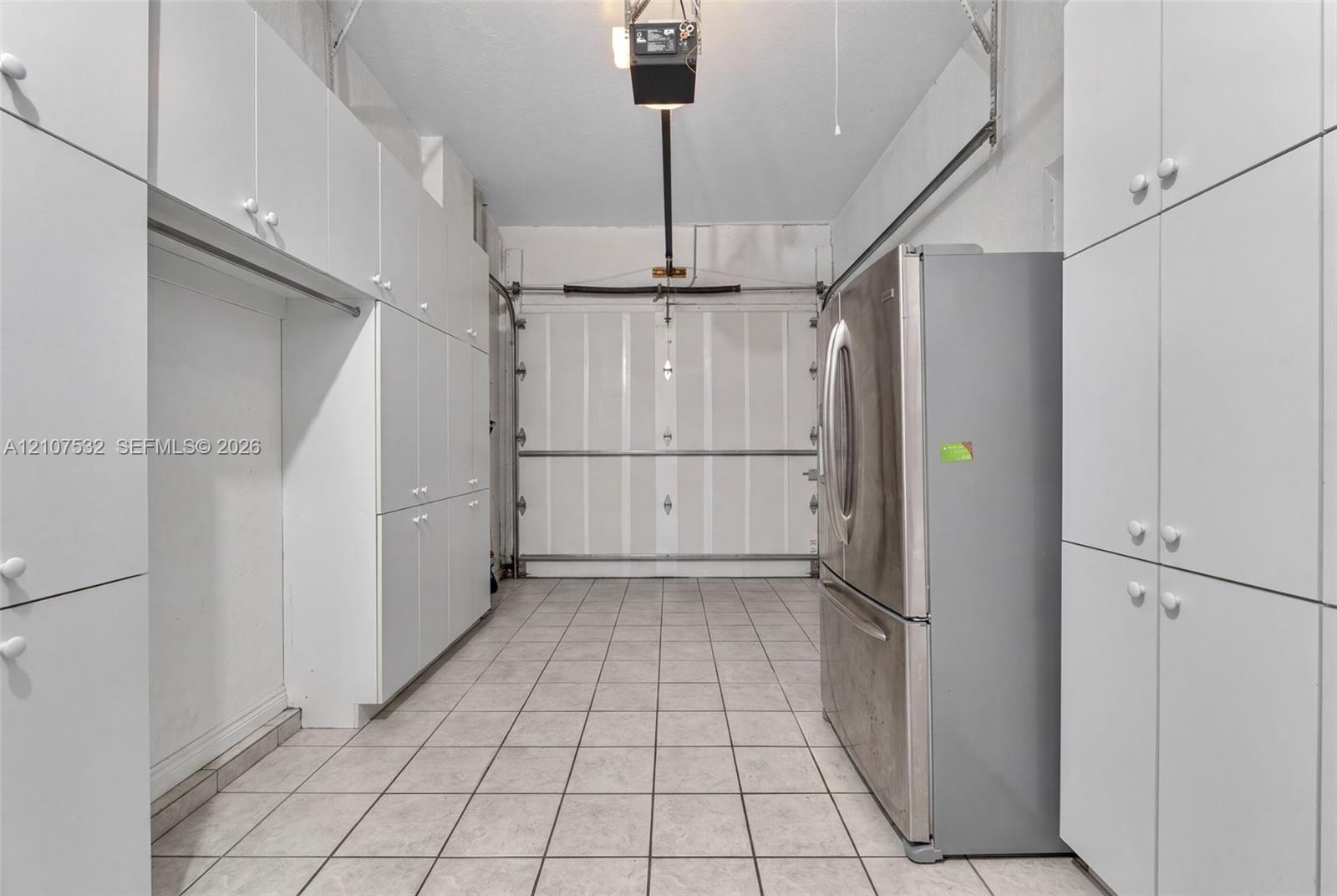 Enclosed garage featuring extensive wall-to-wall built-in cabinetry, ceramic tile flooring, and a stainless steel refrigerator