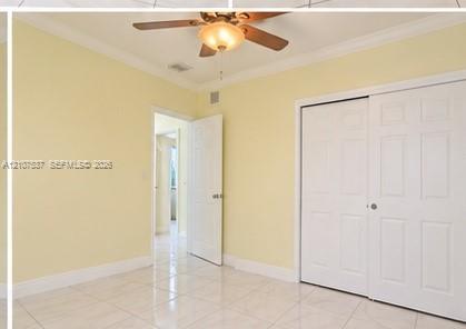Room featuring light-toned tile flooring, white six-panel closet doors, crown molding, and a ceiling fan with integrated lighting Room featuring light-toned tile flooring, white six-panel closet doors, crown molding, and a ceiling fan with integrated lighting