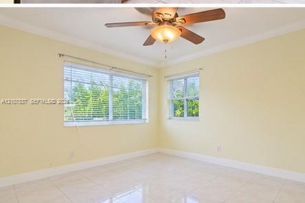 Room featuring light-toned tile flooring, crown molding, a central ceiling fan with integrated light fixture, and dual windows with horizontal blinds Room featuring light-toned tile flooring, crown molding, a central ceiling fan with integrated light fixture, and dual windows with horizontal blinds