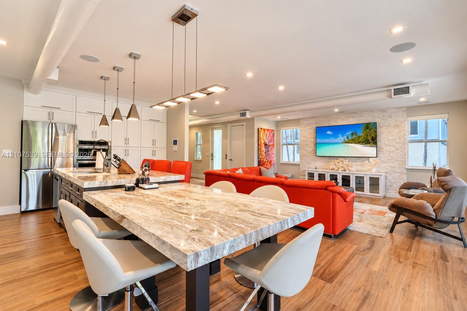 Open-concept interior featuring stone-surface island seating, stainless steel appliances, stacked-stone accent wall, recessed lighting, and wood-finish flooring
